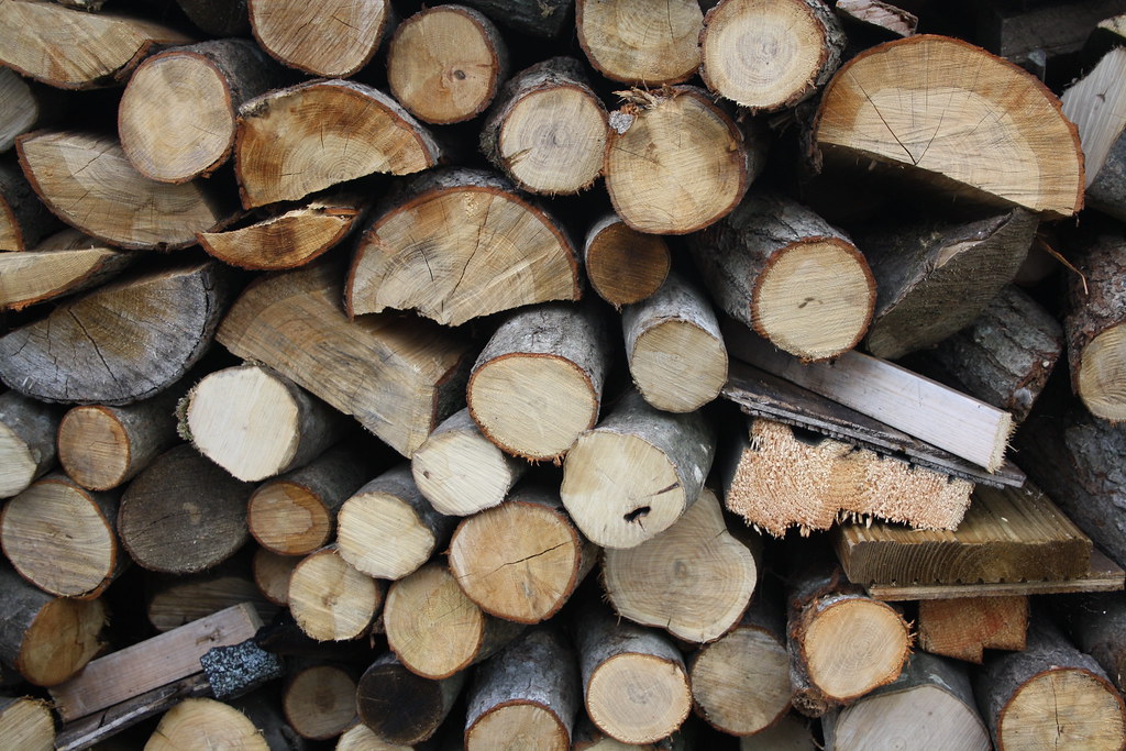 Stacked firewood logs from tree cleanup work, ready for splitting